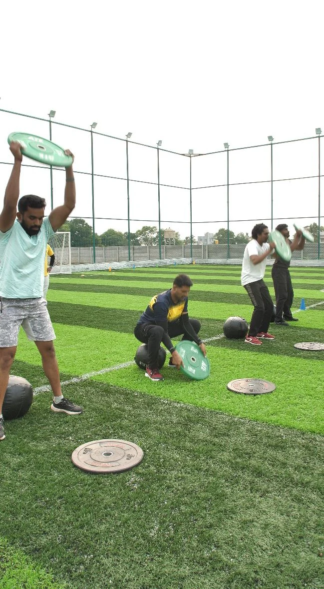 Members lifting weight plates overhead during an outdoor session on the turf
